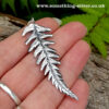 Sterling silver fern pendant with a silver belcher chain on a natural background whilst held in a hand