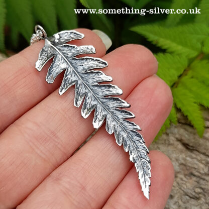 reverse of Sterling silver fern pendant with a silver belcher chain on a natural background whilst held in a hand