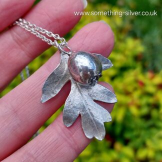 Sterling silver hawthorn leaf and berry in hand with natural background