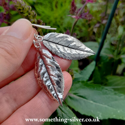 sterling silver rose leaf drop earrings held in hand with natural background