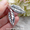 sterling silver rose leaf drop earrings held in hand with flower background