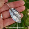 Sterling silver rose leaf pendant on belcher chain. Held in had over a natural background