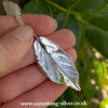 Sterling silver rose leaf pendant on belcher chain. Held in had over a natural background, reverse side